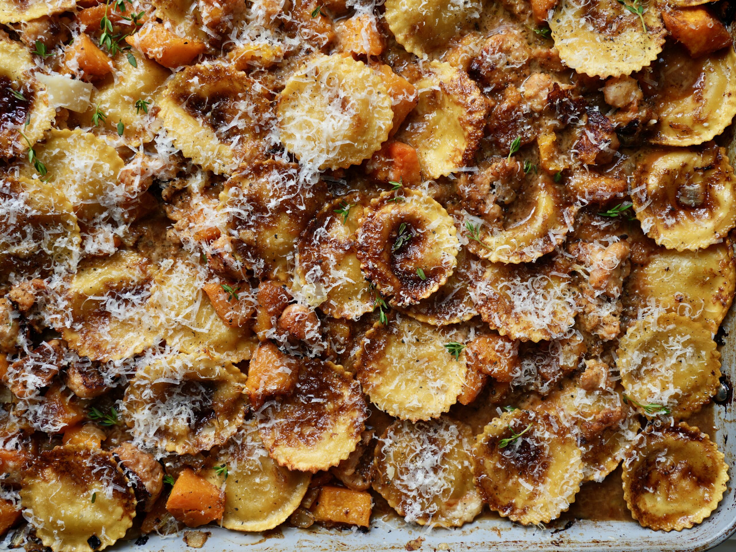 Overhead view of browned ravioli and sausage with butternut squash in creamy sauce, finished with Parmesan and thyme.