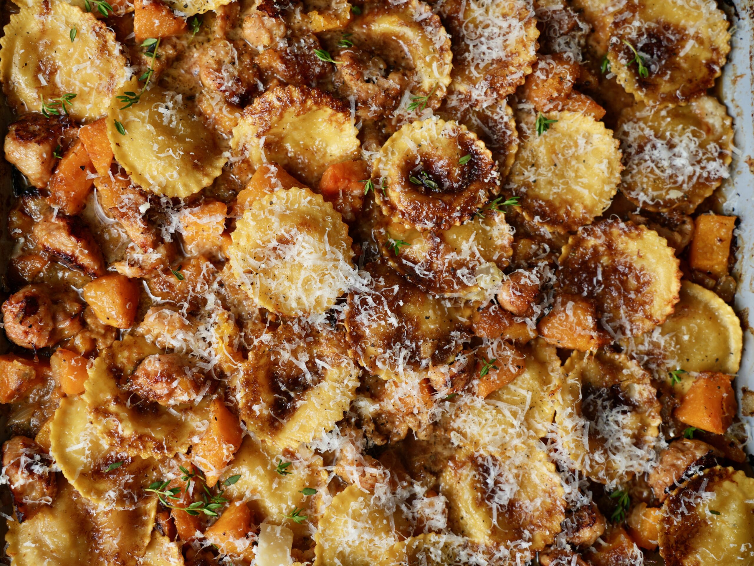 Close-up of golden ravioli, browned sausage and roasted butternut squash topped with grated Parmesan and thyme.